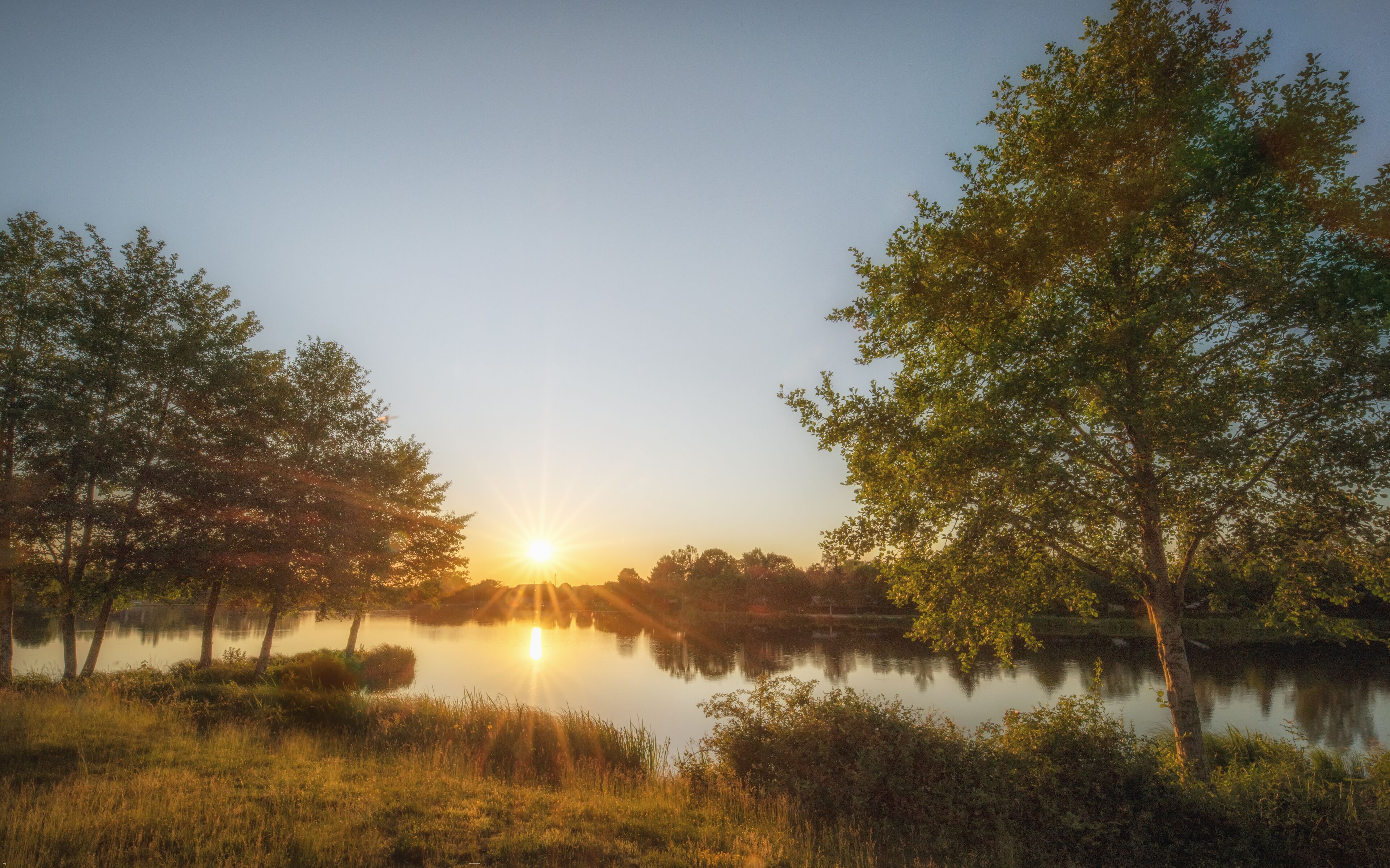 A sunset over a calm lake with trees reflecting the sky.