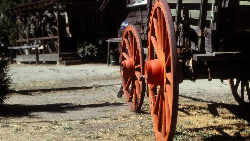 A vintage wooden building with a metal roof and two large orange wheels in front.