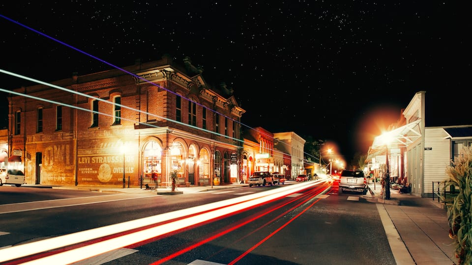 A nighttime street scene with illuminated buildings and light trails from moving vehicles.