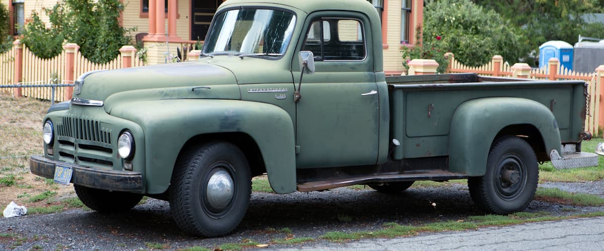 A vintage green pickup truck parked in front of a house with a porch.