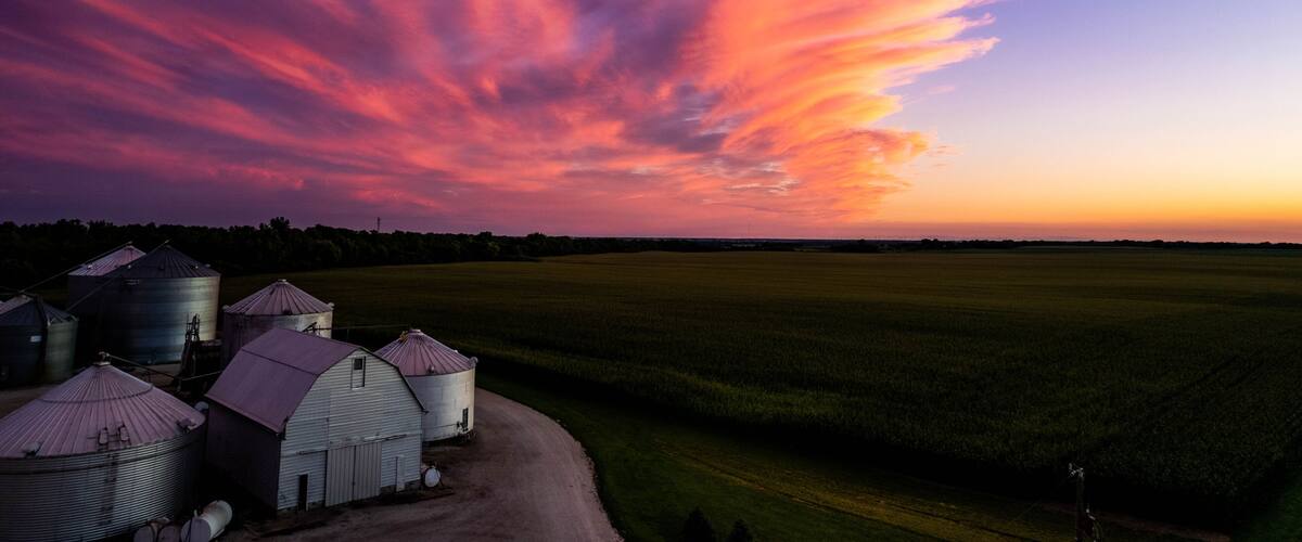 A sunset over a rural landscape with silos and a field.