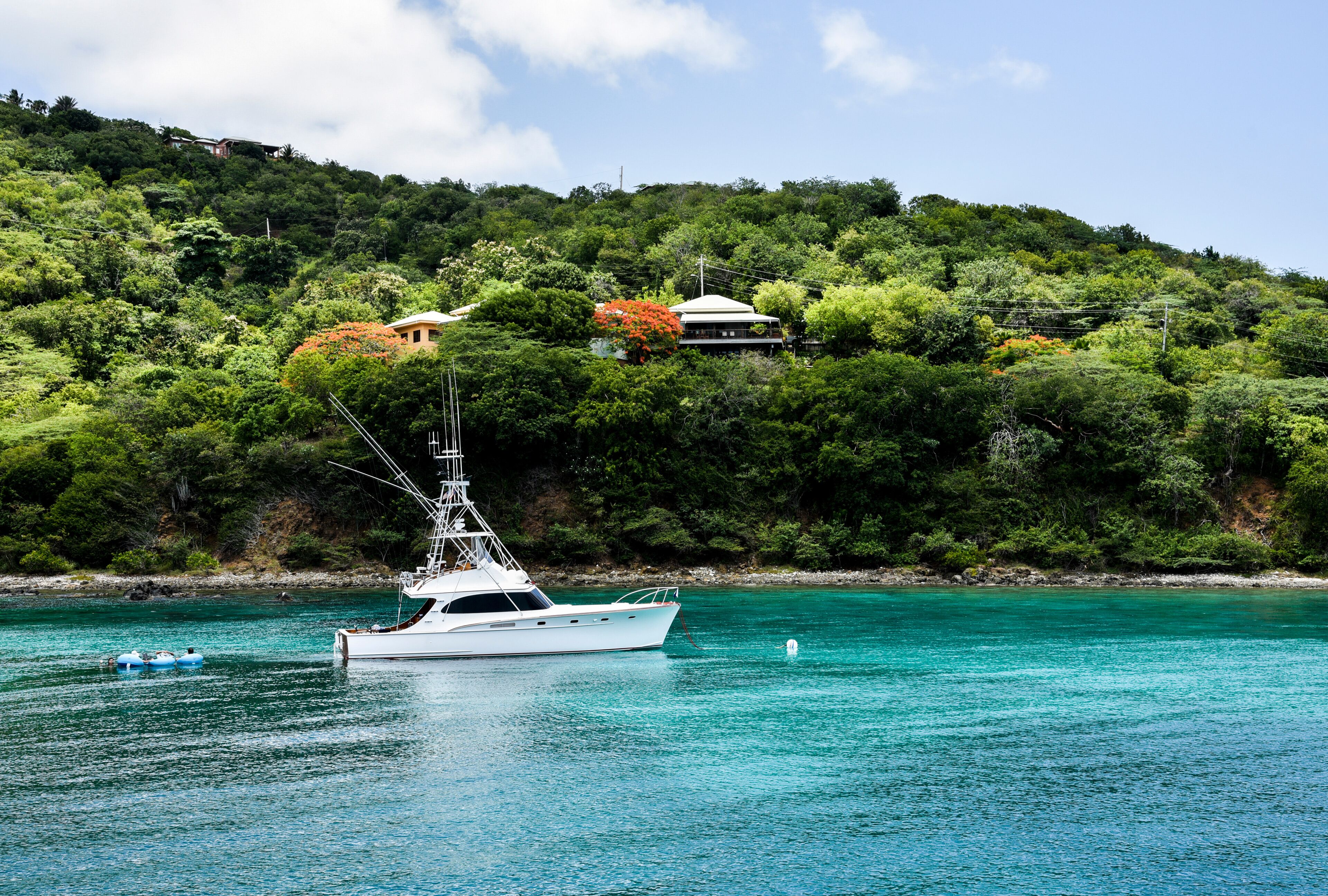 A white yacht on turquoise waters with a lush green hillside in the background.