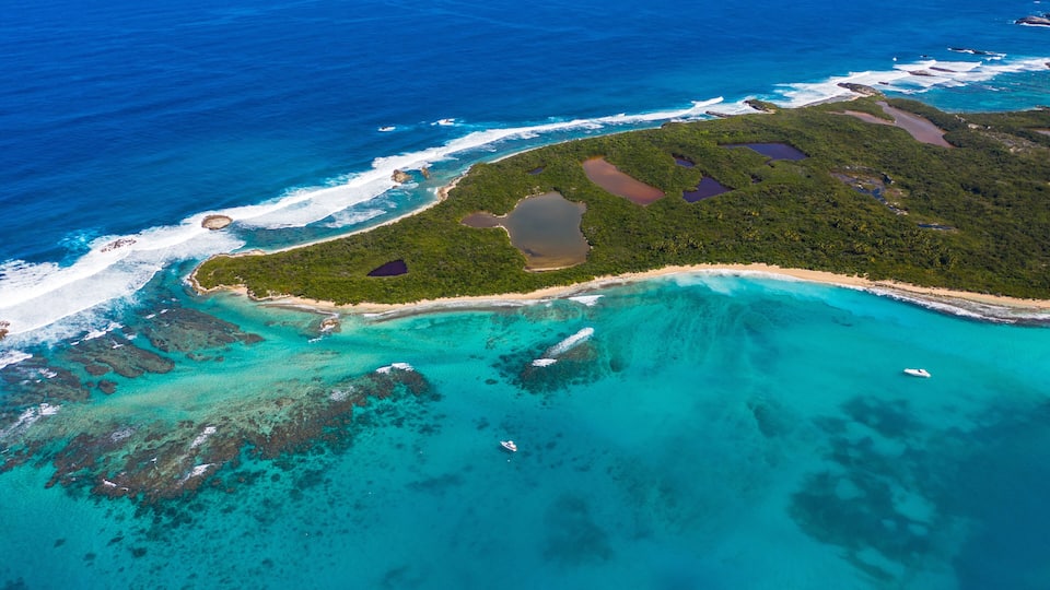 An aerial view of a tropical island with clear turquoise waters, a sandy beach, and lush green vegetation.