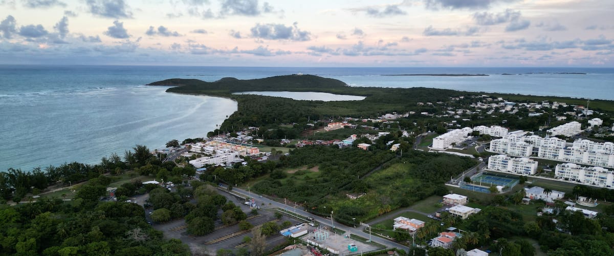 A coastal town with a beach, residential buildings, and a hilly landscape.