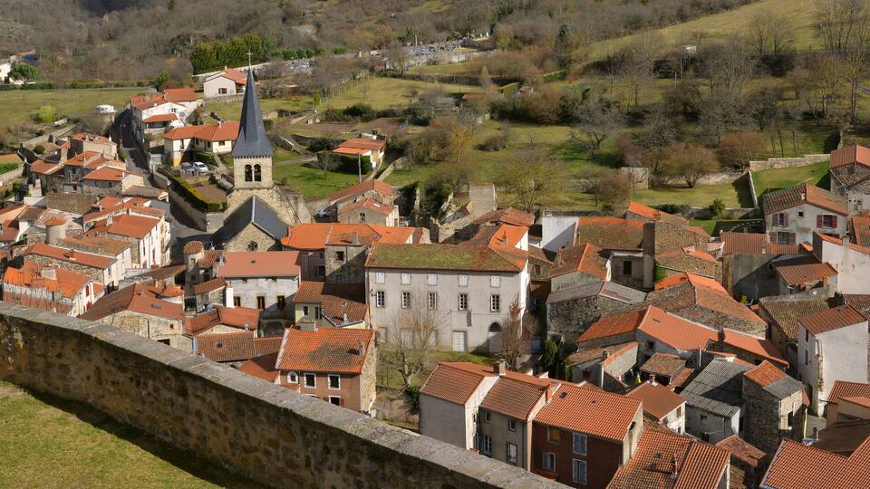A historic town with red-tiled roofs, a prominent church tower, and a stone wall.