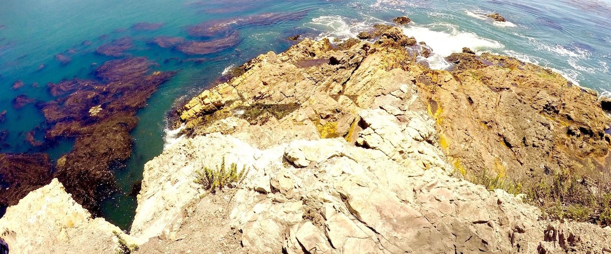 A coastal landscape with rocky cliffs, clear blue waters, and distant mountains.