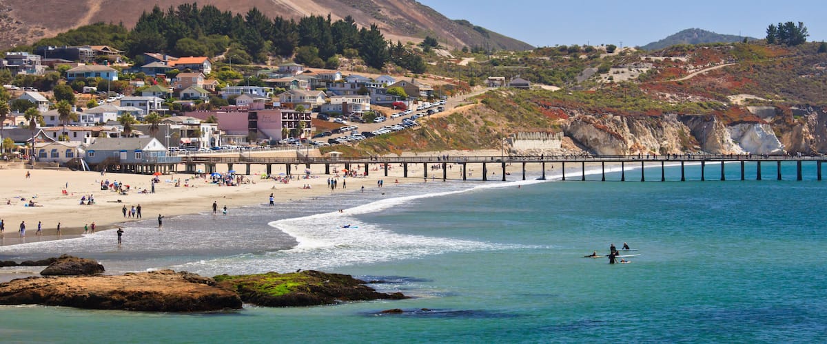A coastal town with a beach, pier, and hills in the background.