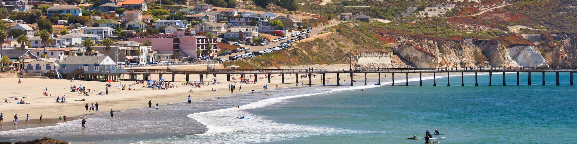A coastal town with a beach, pier, and hills in the background.