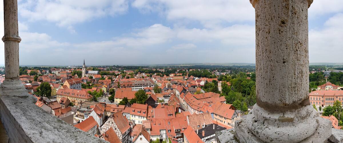 A view from a stone balcony overlooking a town with red-roofed buildings and a distant church spire.