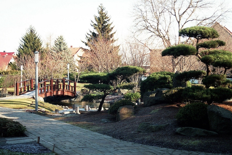 A landscaped garden with a wooden bridge, neatly trimmed trees, and a pond.