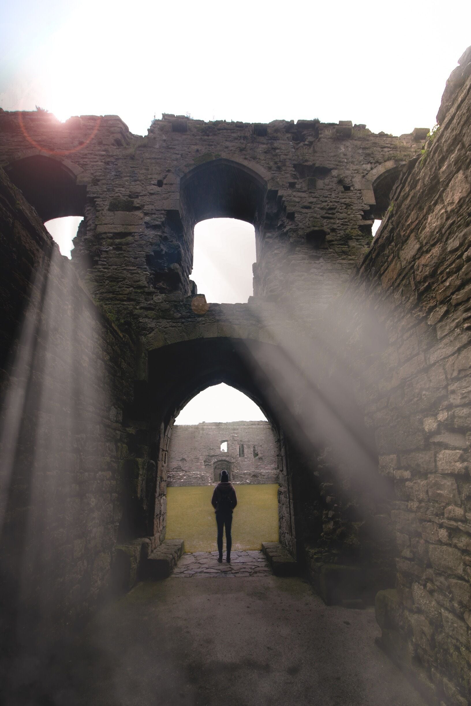 A person standing in a stone archway with sunlight streaming through.