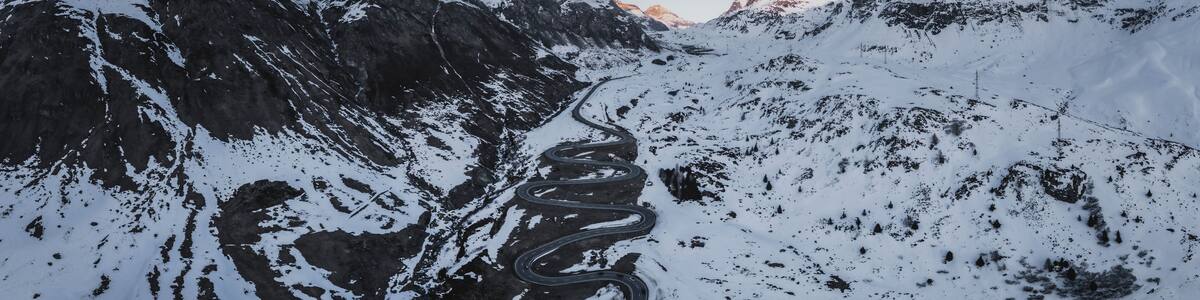 Aerial view of breathtaking panoramic landscape with snow-covered mountains and a winding road at sunset, Julierpass, Grisons, Switzerland.