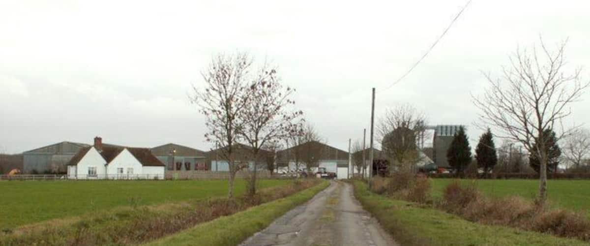 A rural road with farm buildings and open fields.