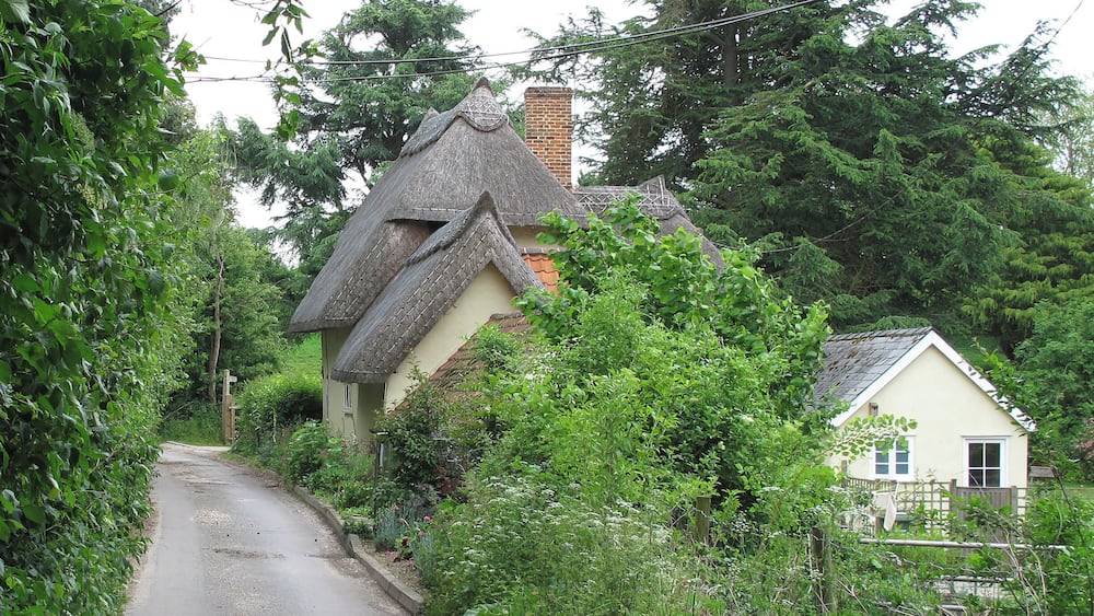 Une route étroite bordée d’une végétation luxuriante et de maisons traditionnelles aux toits de chaume.