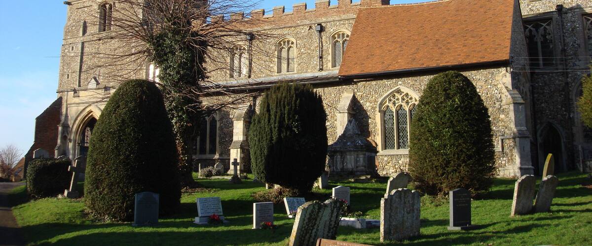 A historic church with a clock tower, surrounded by well-maintained graveyard and hedges.