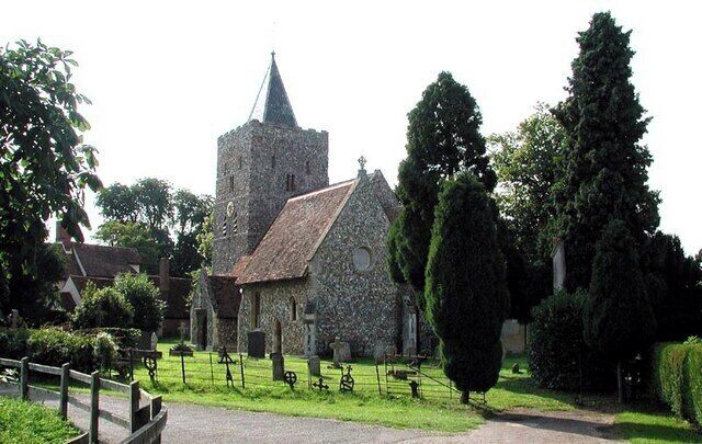 A stone church with a bell tower, surrounded by a cemetery with headstones and tall trees.