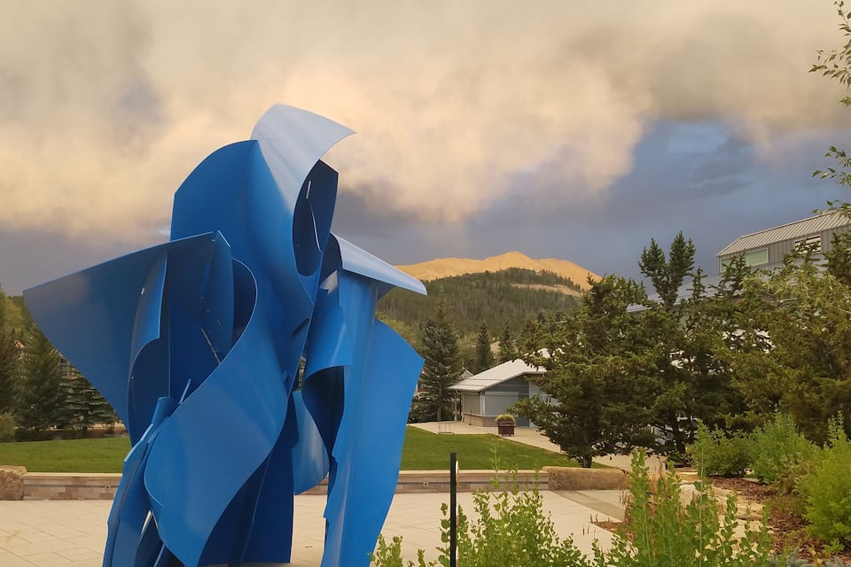 Een blauwe abstracte sculptuur in een park, met een berg op de achtergrond.