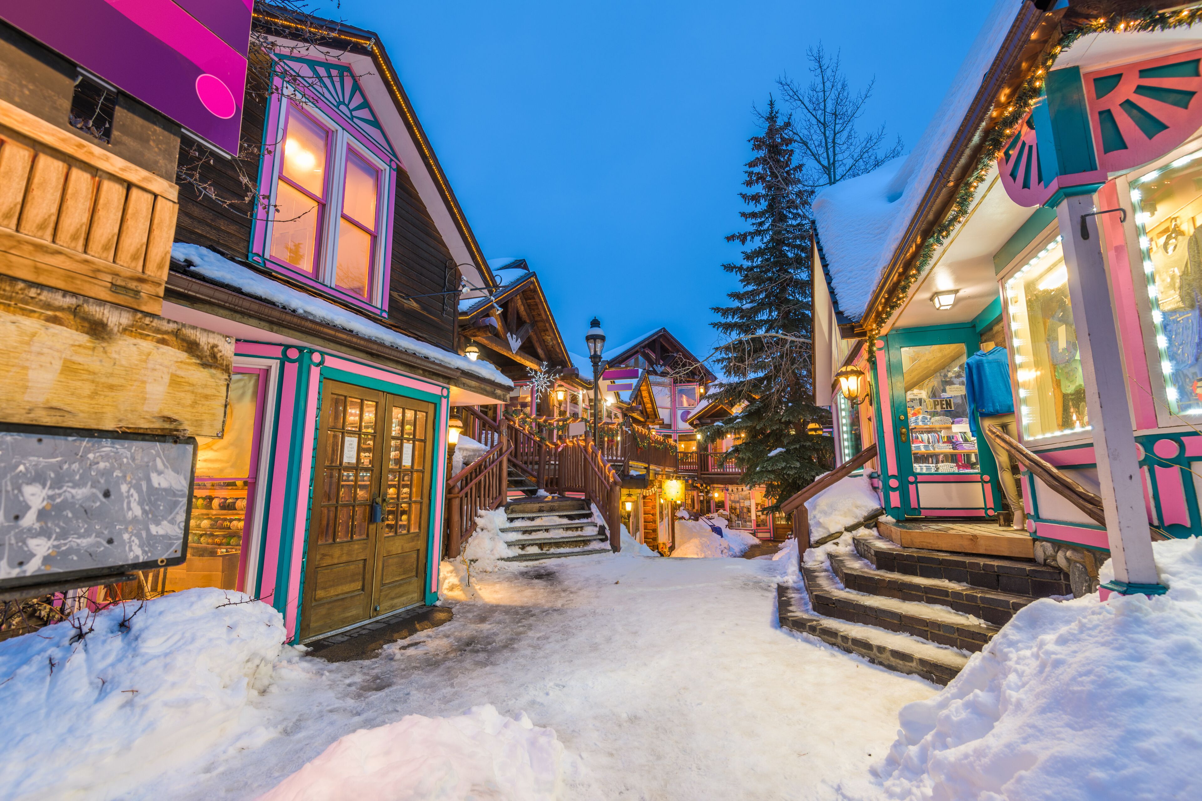 A snow-covered street with wooden buildings and a brightly lit shop.