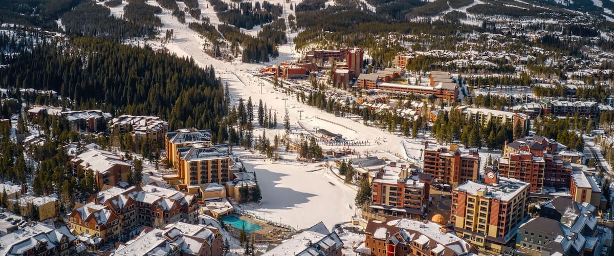A snow-covered mountain town with ski slopes, buildings, and a clear sky.