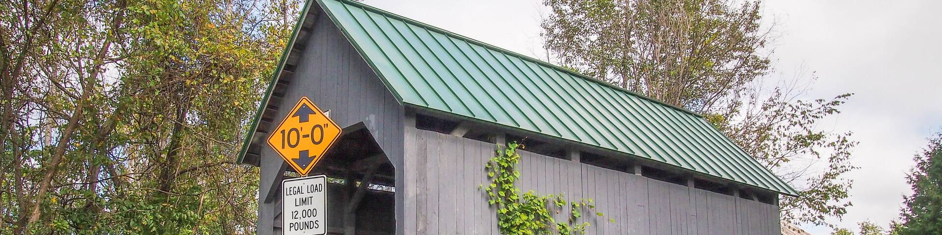 A covered bridge with a green roof, a 10-0' clearance sign, and a legal load limit sign.