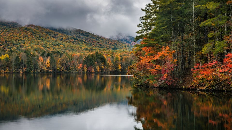 A calm lake surrounded by autumn-colored trees and a misty mountain backdrop.