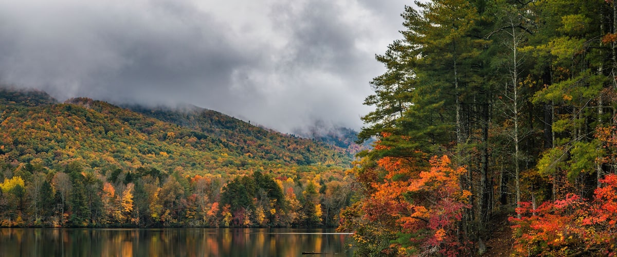 A calm lake surrounded by autumn-colored trees and a misty mountain backdrop.