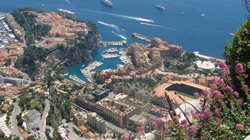 A coastal city with a marina, historic buildings, and a mountainous backdrop.