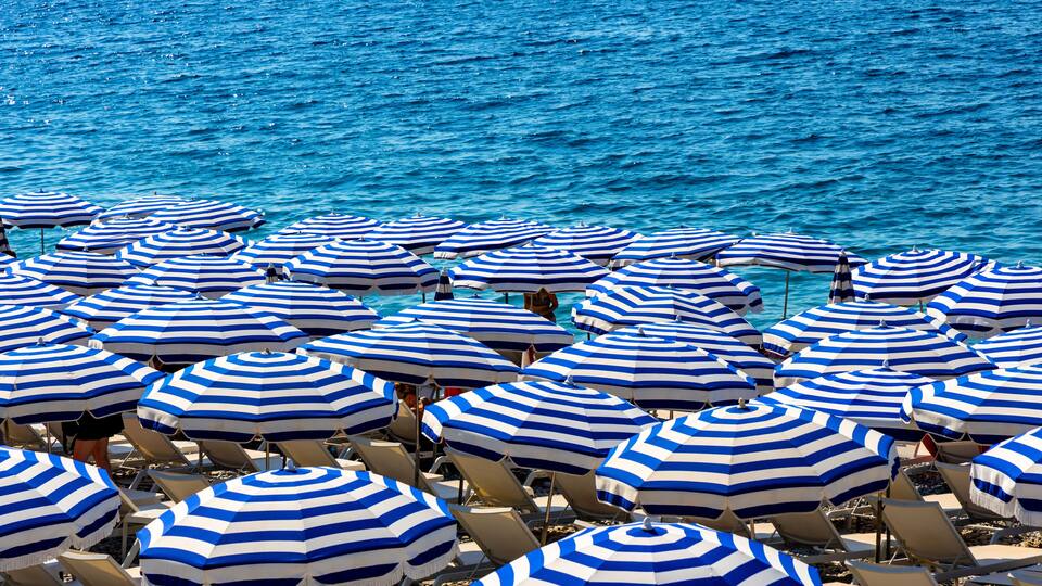 A beach with numerous blue and white striped umbrellas and sun loungers.