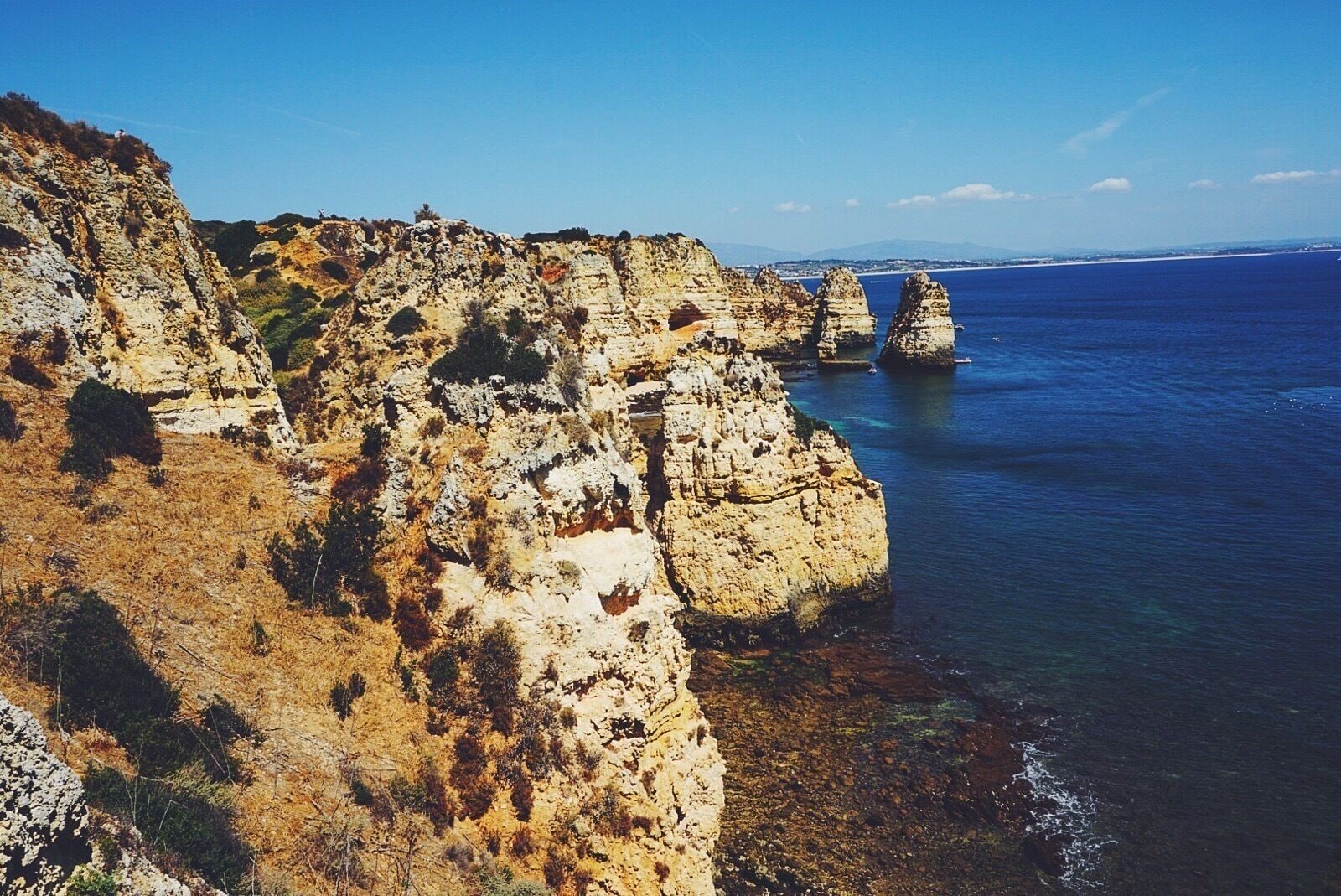 Une falaise côtière aux formations rocheuses stratifiées, surplombant une mer bleue et limpide.