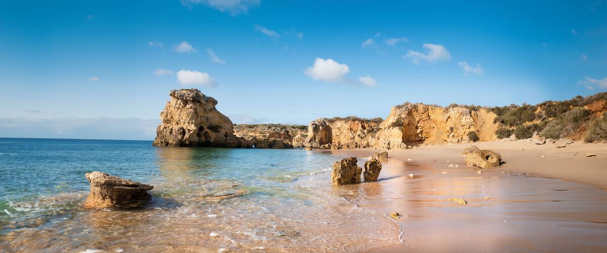 A coastal landscape with clear waters, rocky formations, and a sandy beach.