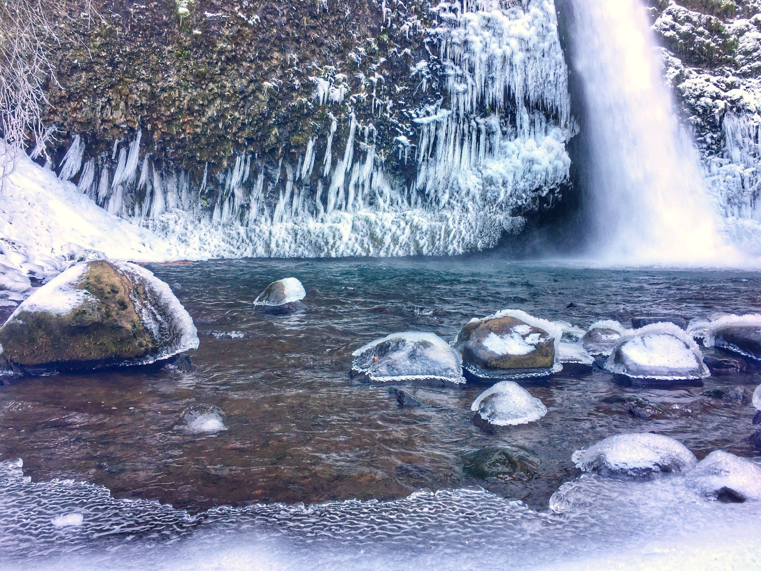 A frozen waterfall with icicles and snow-covered rocks in a clear stream.