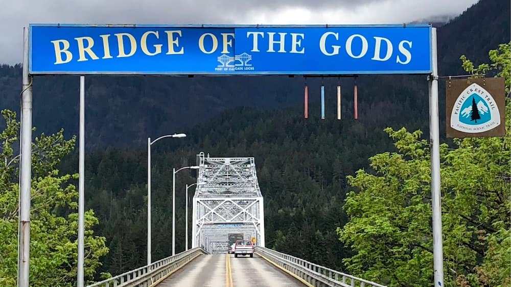 Un pont sur lequel est affiché un panneau indiquant « Pont des dieux » et un autre panneau indiquant le tracé du sentier Pacific Crest.