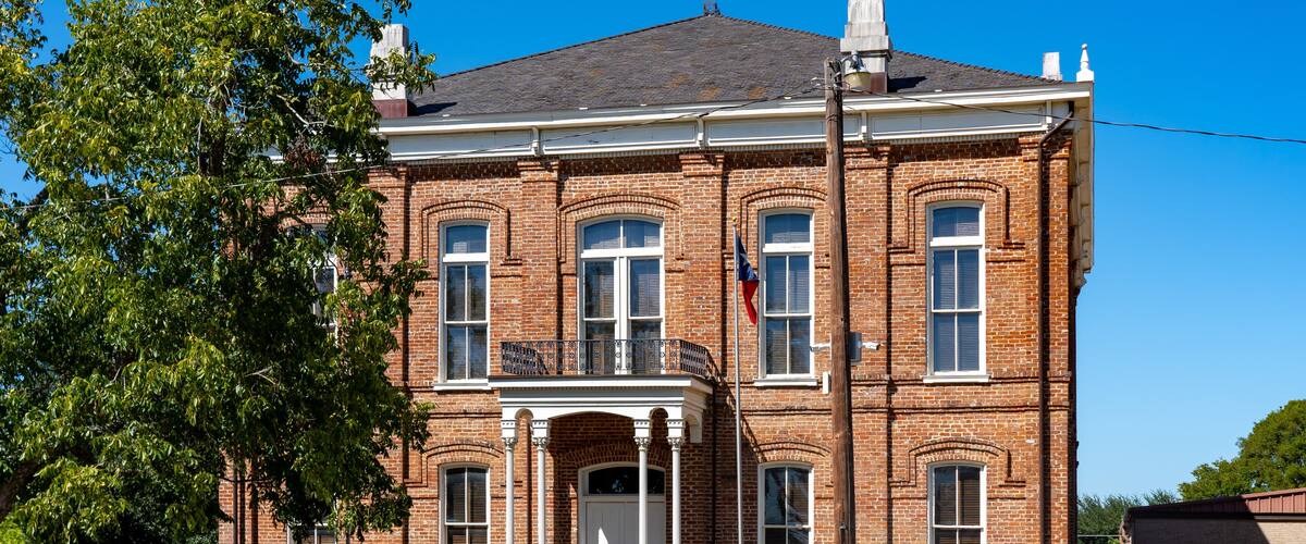 A large brick building with a balcony, a flag, and a flagpole.