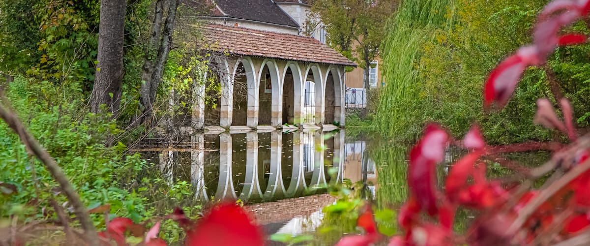 A historic building with a tiled roof, surrounded by lush greenery and a reflective pond.
