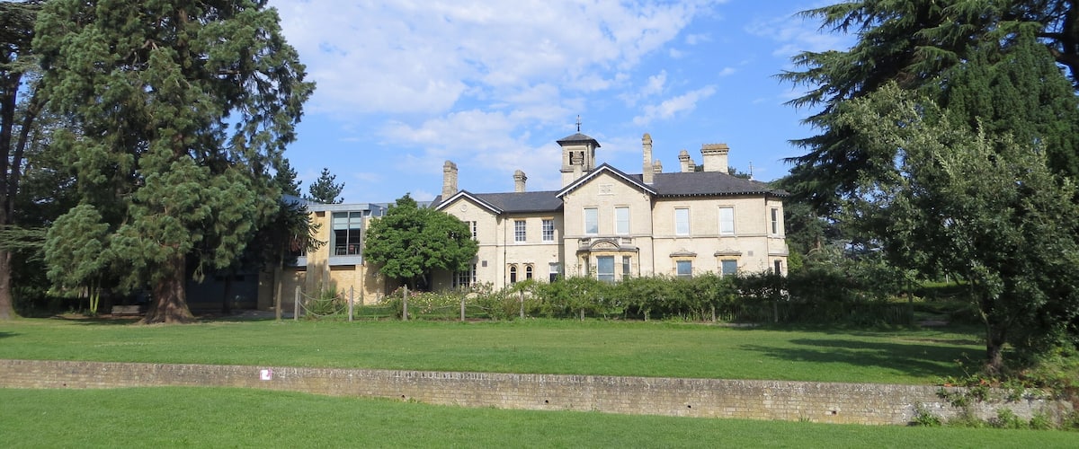 A large, historic building with multiple chimneys and a prominent tower, surrounded by lush green grass and trees.