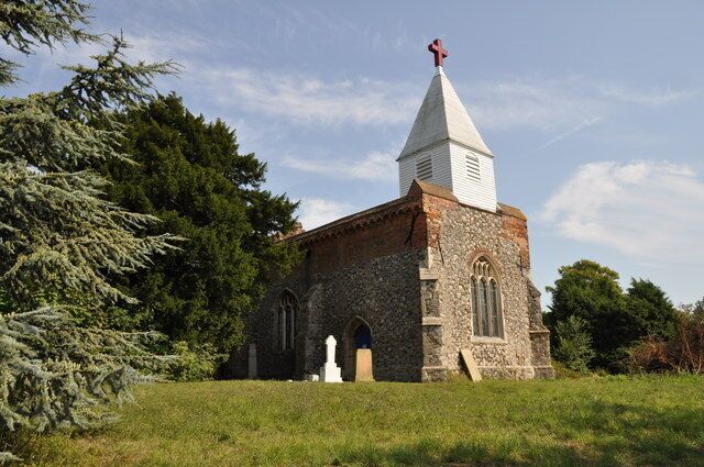 A small stone church with a white steeple and a red cross on top, surrounded by trees and grass.