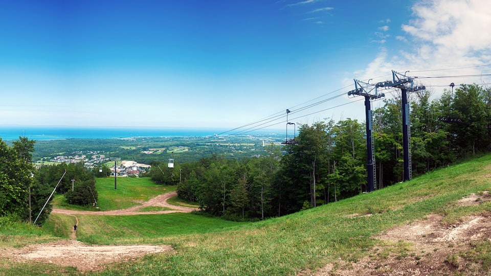 A scenic view of a hilly landscape with a dirt path leading to a viewpoint overlooking a coastal town and the ocean.