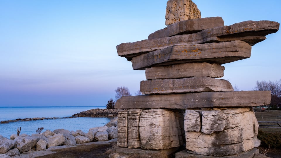A stone totem with stacked layers, situated by a body of water.