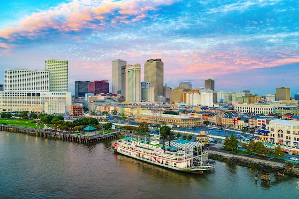 A river with a steamboat, a city skyline with various buildings, and a sunset sky.