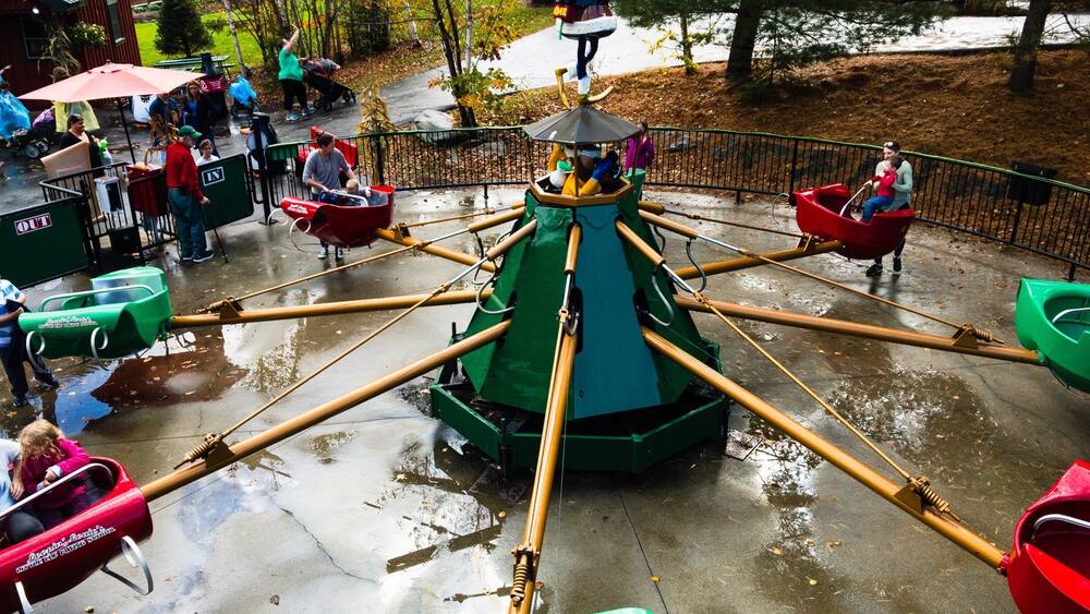 Une attraction aquatique avec des bateaux verts et rouges, une structure centrale rotative et un sol mouillé.