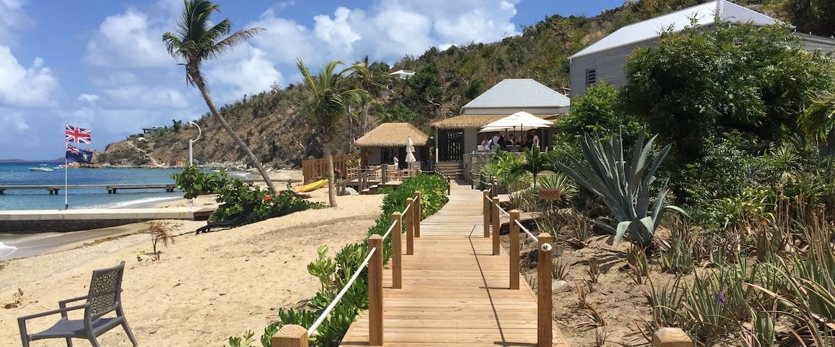 A wooden boardwalk leading to a beach with palm trees and a thatched-roof hut.