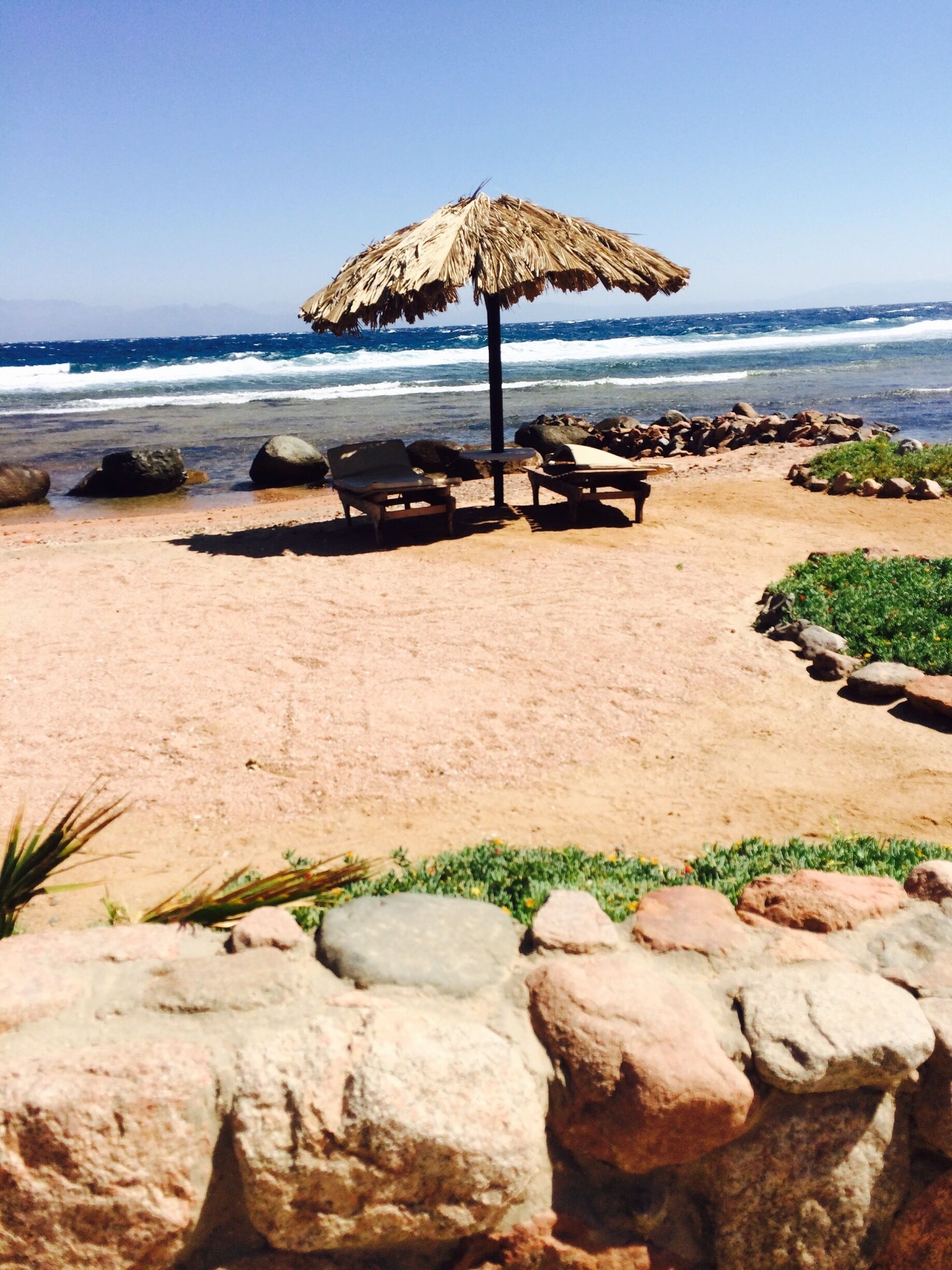 Una playa con una sombrilla de paja, sillas de descanso y costa rocosa.