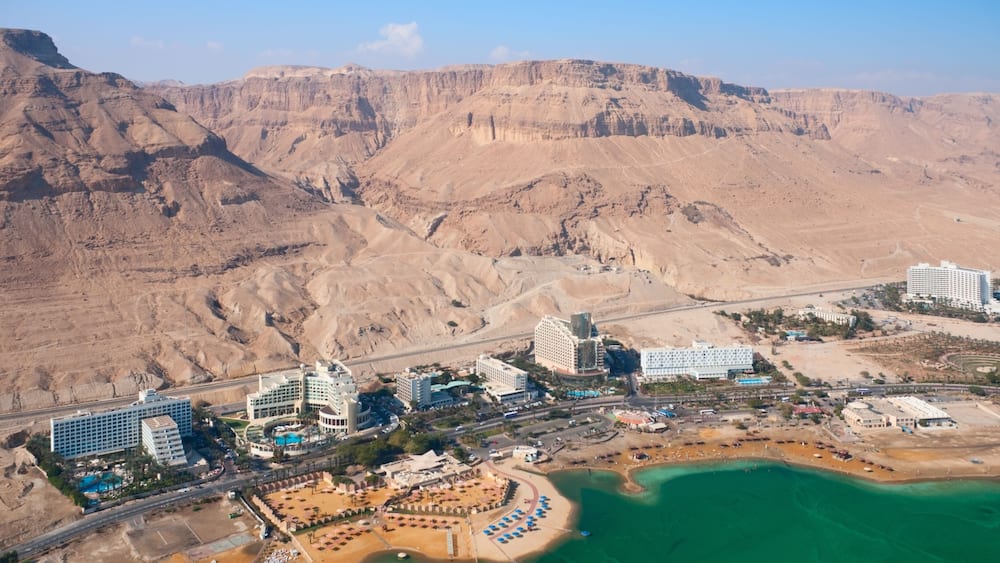 An aerial view of a coastal resort with buildings, a beach, and a desert landscape in the background.
