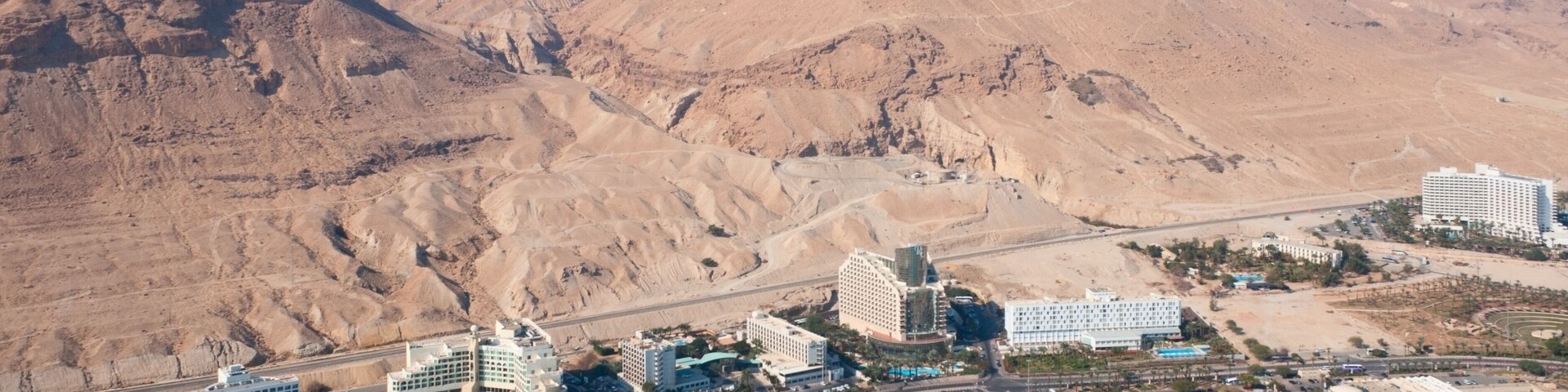 Vista aérea de un complejo turístico costero con edificios, una playa y un paisaje desértico al fondo.