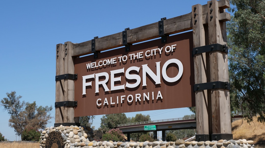 A welcome sign for the City of Fresno, California, with a stone wall and a bridge in the background.