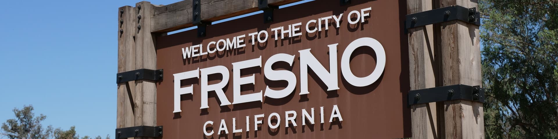 A welcome sign for the City of Fresno, California, with a stone wall and a bridge in the background.