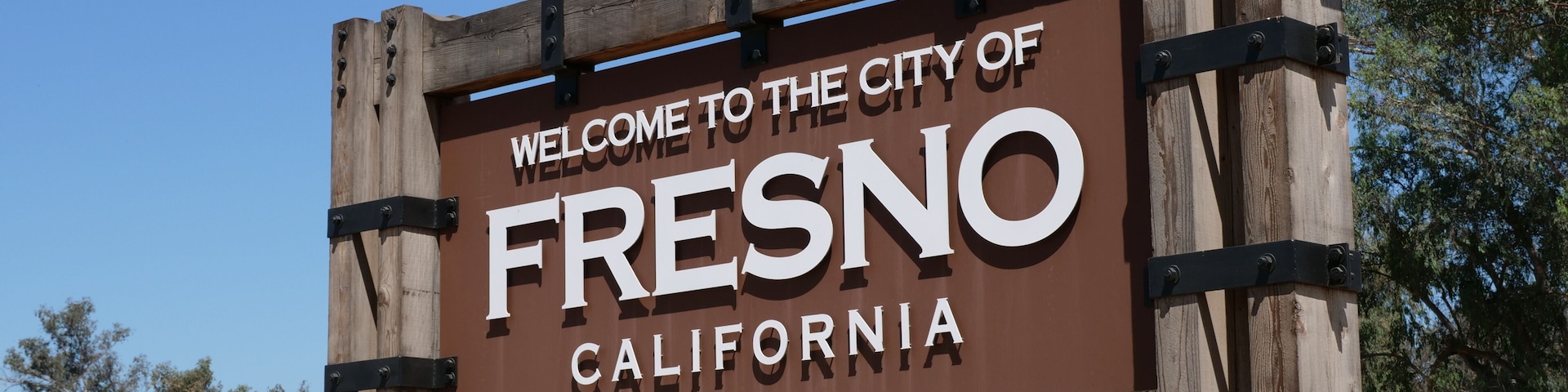 A welcome sign for the City of Fresno, California, with a stone wall and a bridge in the background.