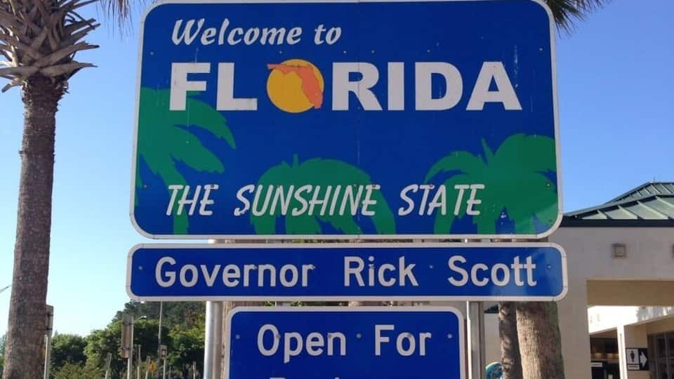 A welcome sign for Florida with palm trees and a clear blue sky.