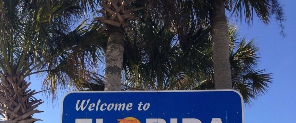 A welcome sign for Florida with palm trees and a clear blue sky.