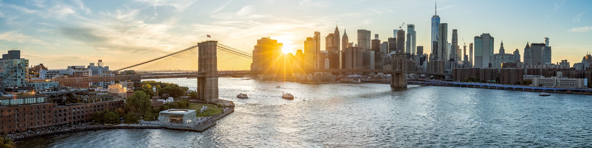 A city skyline with a prominent bridge and skyscrapers, including the Empire State Building, during sunset.